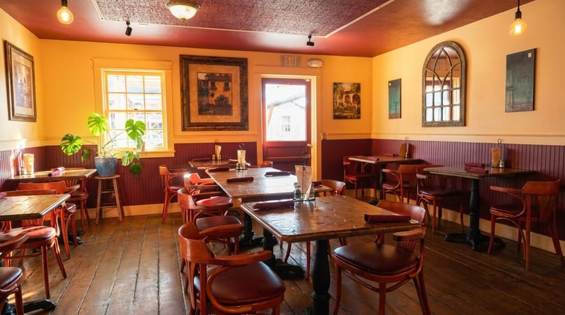 Cozy restaurant interior with wooden tables and chairs, yellow walls, and red wainscoting.