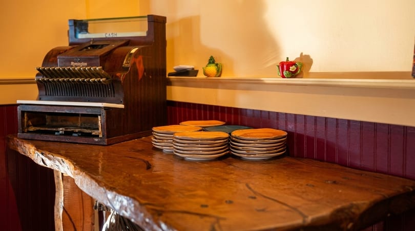 Vintage wooden cash register and stacks of plates on a rustic wooden counter with red wainscoting.